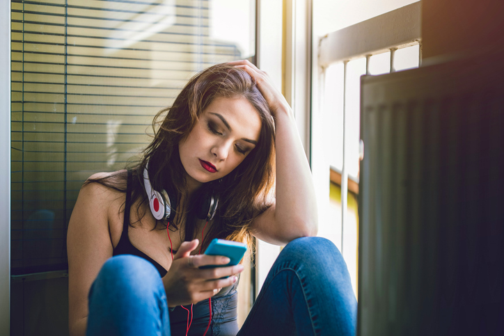 Caucasian woman sitting on floor and using mobile phone