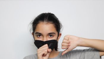 Portrait Of Girl Wearing Pollution Mask Coughing Against White Background