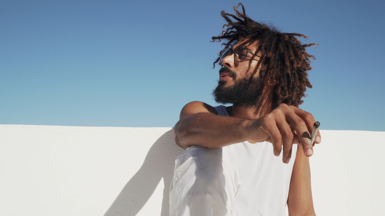 Black man smoking weed at the rooftop with blue sky at background