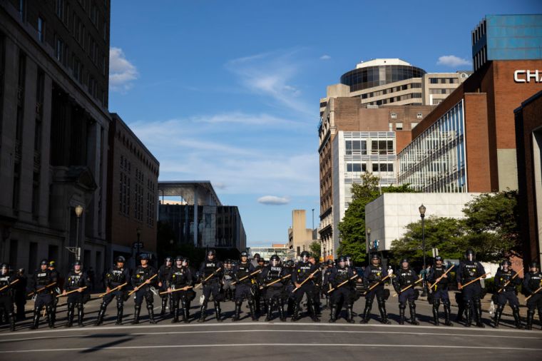 Police officers in riot gear stand in formation at a cross street as they make their way to where protesters are gathered in Louisville.