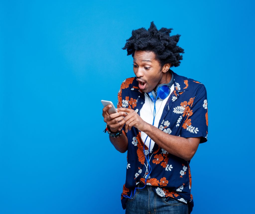 Shocked young man in hawaiian shirt holding smart phone