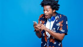 Shocked young man in hawaiian shirt holding smart phone