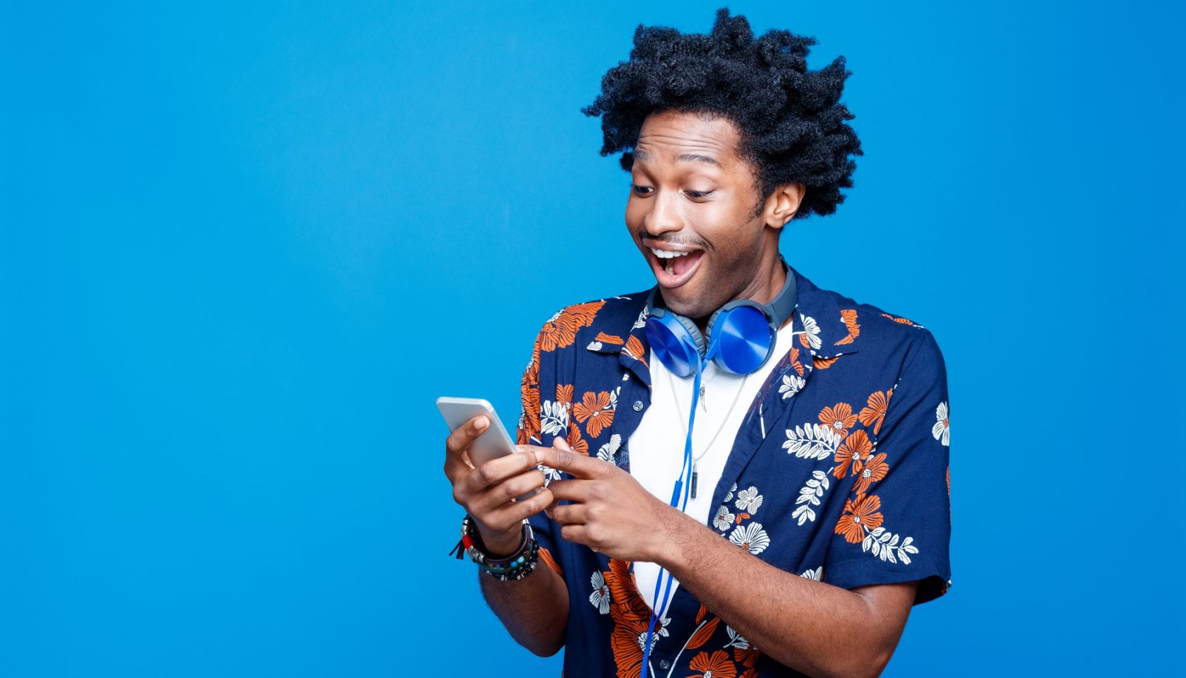 Surprised young man in hawaiian shirt holding smart phone