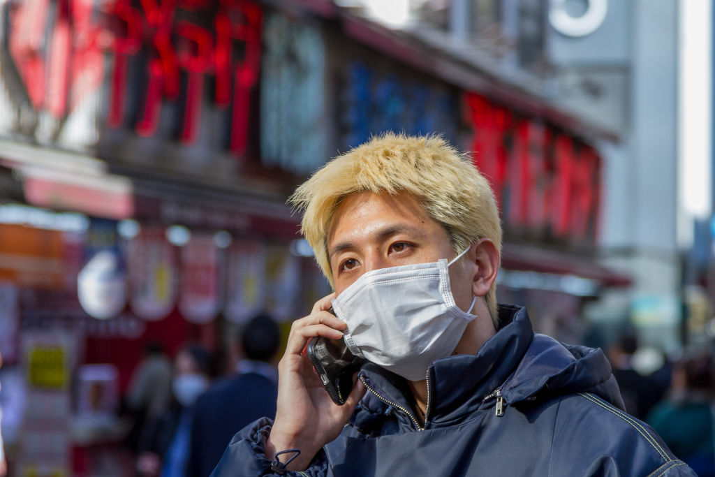 A man with hair dyed blonde wears a face mask as a...