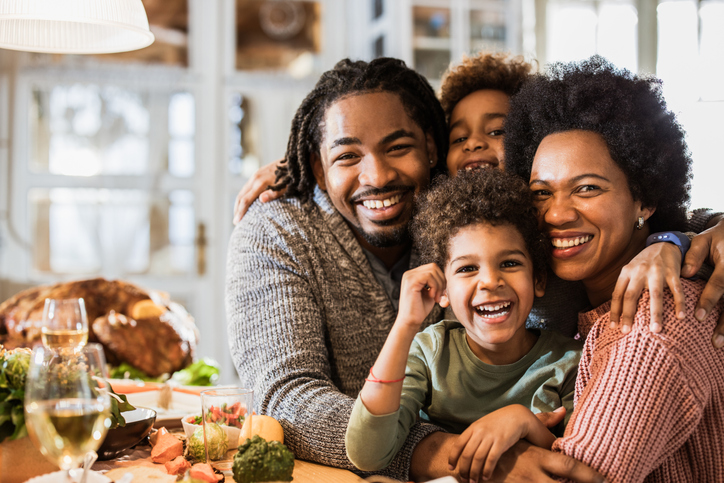 Embraced African American family during Thanksgiving meal at dining table.
