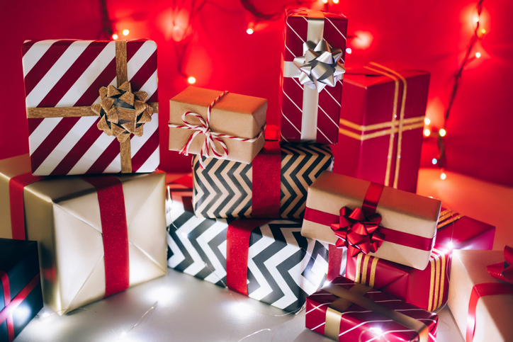 Stack of present boxes wrapped in ornamental paper and illuminated with fairy lights on Christmas day against red background. New Year celebration concept