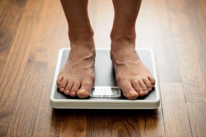 Close-up of weighing on mechanical bathroom scale. Feet standing on weight scale laying on wooden flooring.