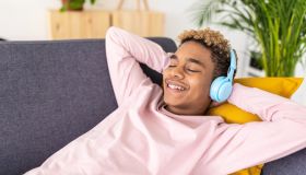 Teenage boy enjoying listening music while relaxing lying on a couch at home.