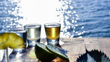 Close-Up Of Tequila Shots With Lemon On Table By Sea