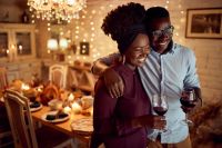 Embraced African American couple drinking while celebrating Thanksgiving at home.