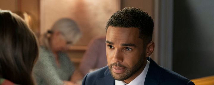 Emily In Paris production still from Season 3 showing Lucien Laviscount as Alfie wearing a blueish gray suit and striped gray tie