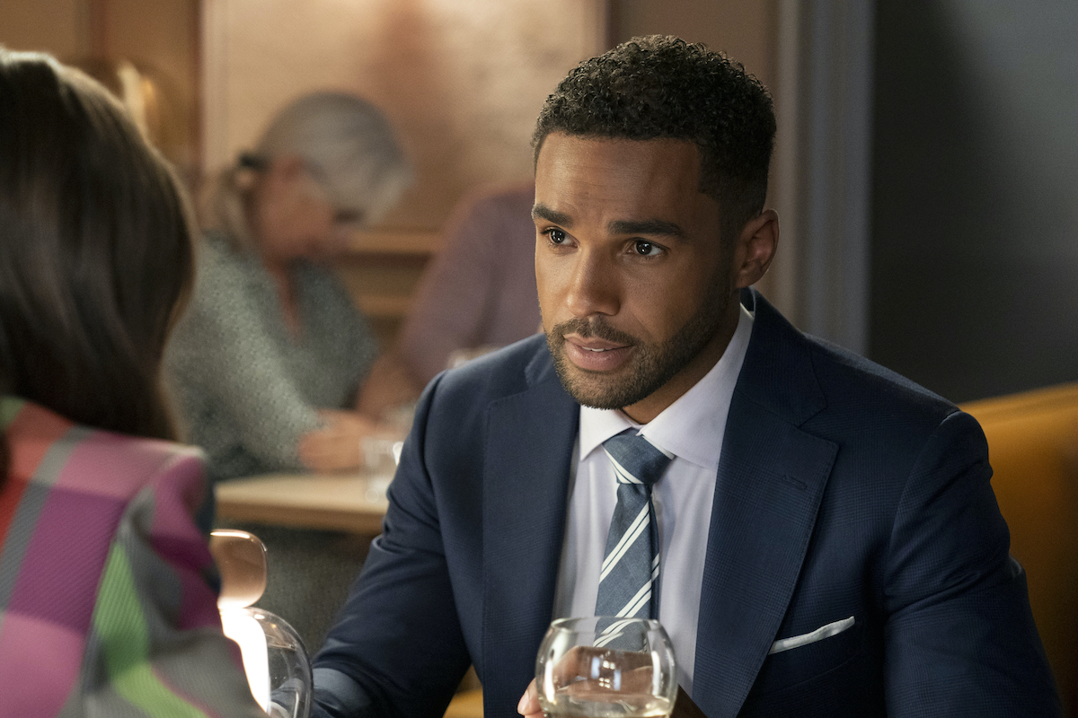 Emily In Paris production still from Season 3 showing Lucien Laviscount as Alfie wearing a blueish gray suit and striped gray tie