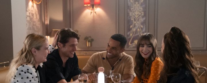 Emily In Paris production still from Season 3 featuring Camille Razat as Camille in a polka dot outfit, Lucas Bravo as Gabriel in a black chef shirt, Lucien Laviscount as Alfie in a tan polo, Lily Collins as Emily in an orange sweater and Ashley Park as Mindy Chen