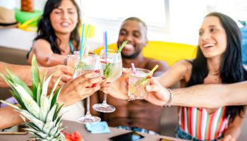 Trendy people toasting fancy cocktails at boat party trip - Young millenial friends having fun on luxury vacation - Travel life style concept with vacationer sharing aperitif drink with tropical fruit