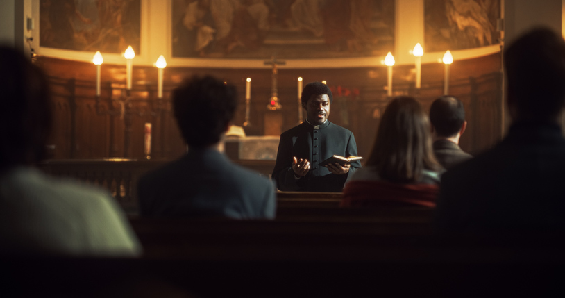 In Christian Church: Portrait of Minister Leading Congregation In Prayer, Reads From Holy Book, The Bible, Gospel of Jesus. Priest Providing Guidance, Belief, Hope, Faith to People. Cinematic Light