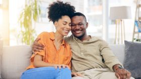 Happiness, love and couple hug, relax and bonding together on lounge couch with partner care, support and trust. Smile, home wellness and black man, woman or marriage people hugging in South Africa