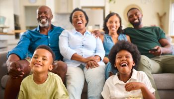 Multi-Generation Family Sitting On Sofa At Home Watching TV Together