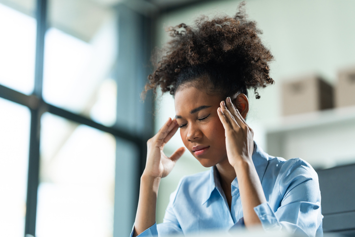 A young African American woman with Afro brown hair in a modern office experiencing panic, business-related stress, frustration, and anxiety.