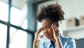 A young African American woman with Afro brown hair in a modern office experiencing panic, business-related stress, frustration, and anxiety.
