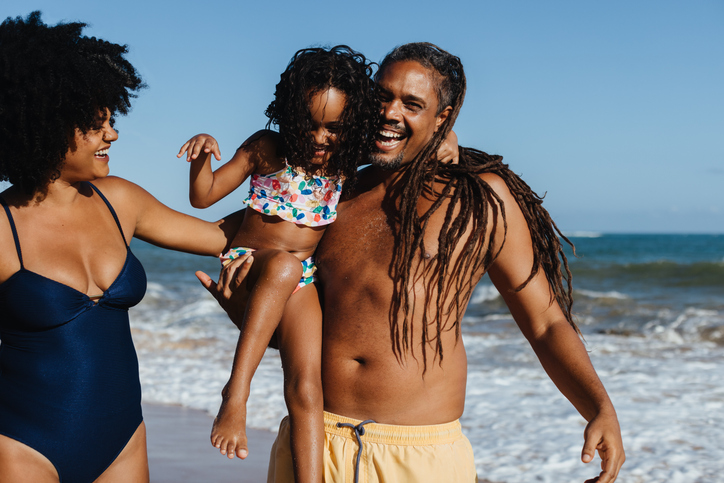 Happy family enjoying summer beach fun with mother, father, and daughter laughing
