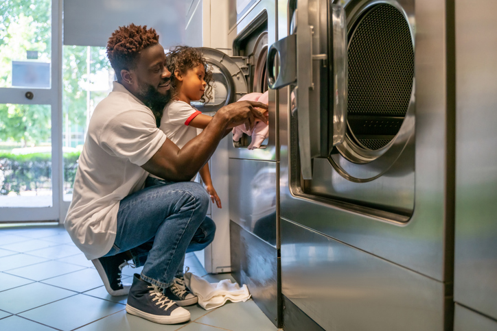 Father and daughter loading laundry into a washer