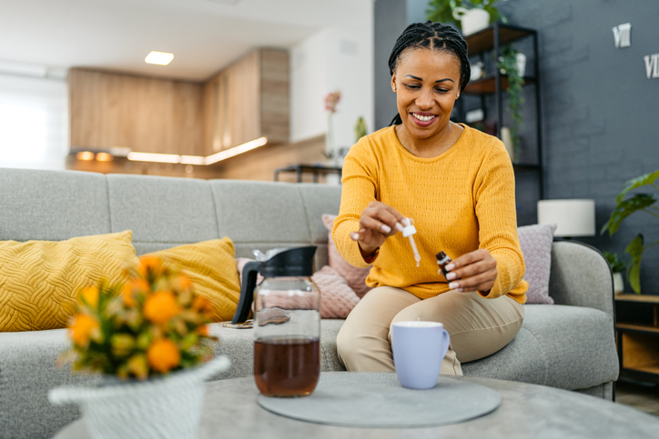 Young Woman Putting Medicine Drops In A Cup Of Tea