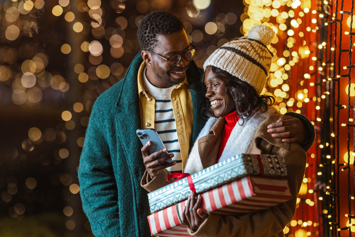 Couple enjoying a festive Christmastime evening outdoors and using a smartphone
