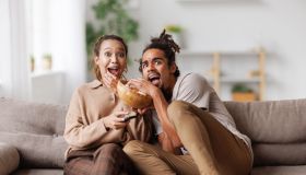 Young scared african american family couple screaming while watching horror movie at home
