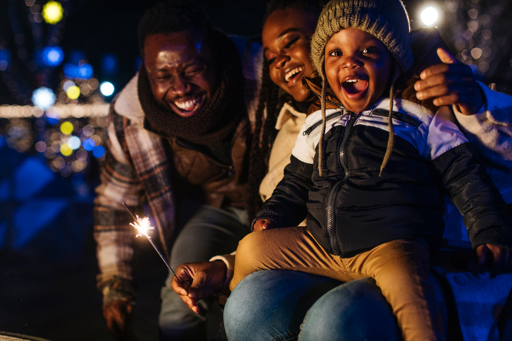 Happy Family And Friends Celebrate With Sparkler At Night, Child On Lap Laughing Together