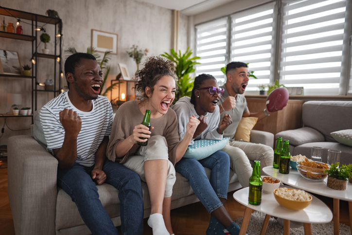 Diverse friends cheering loudly watching American football on TV