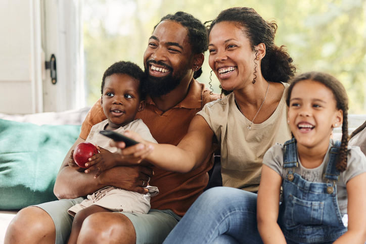 Happy black family watching TV on sofa at home.