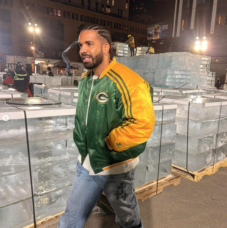 A man wearing a green and yellow Packers jacket stands in front of a set of ice sculptures at what appears to be a television studio or event.