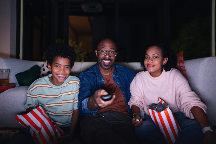 Family Together on Couch Watching Movie Night at Home in the Evening, Smiling and Relaxed