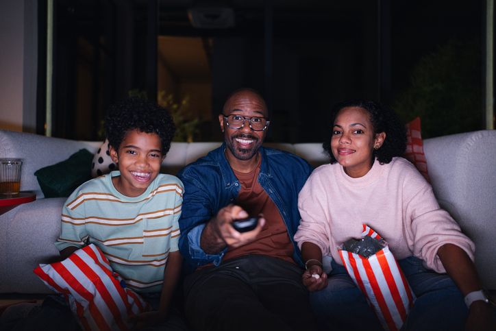 Family Together on Couch Watching Movie Night at Home in the Evening, Smiling and Relaxed