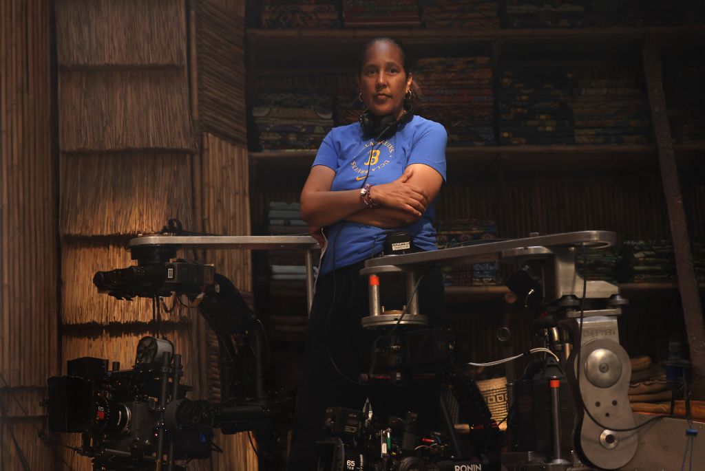 A woman in a blue shirt stands in a film production studio, surrounded by cameras and equipment.