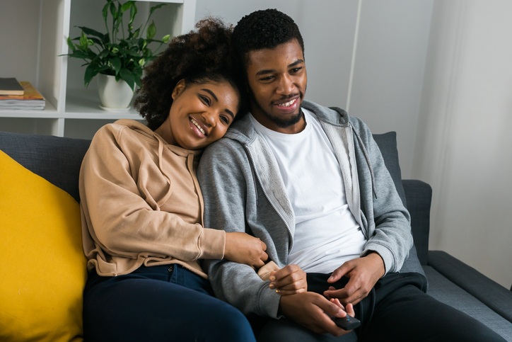 African American couple wife husband watching movie. Family pastime and leisure, watch television, rest. Relaxed man and woman watching TV series together sitting on couch at home enjoying eating popcorn.