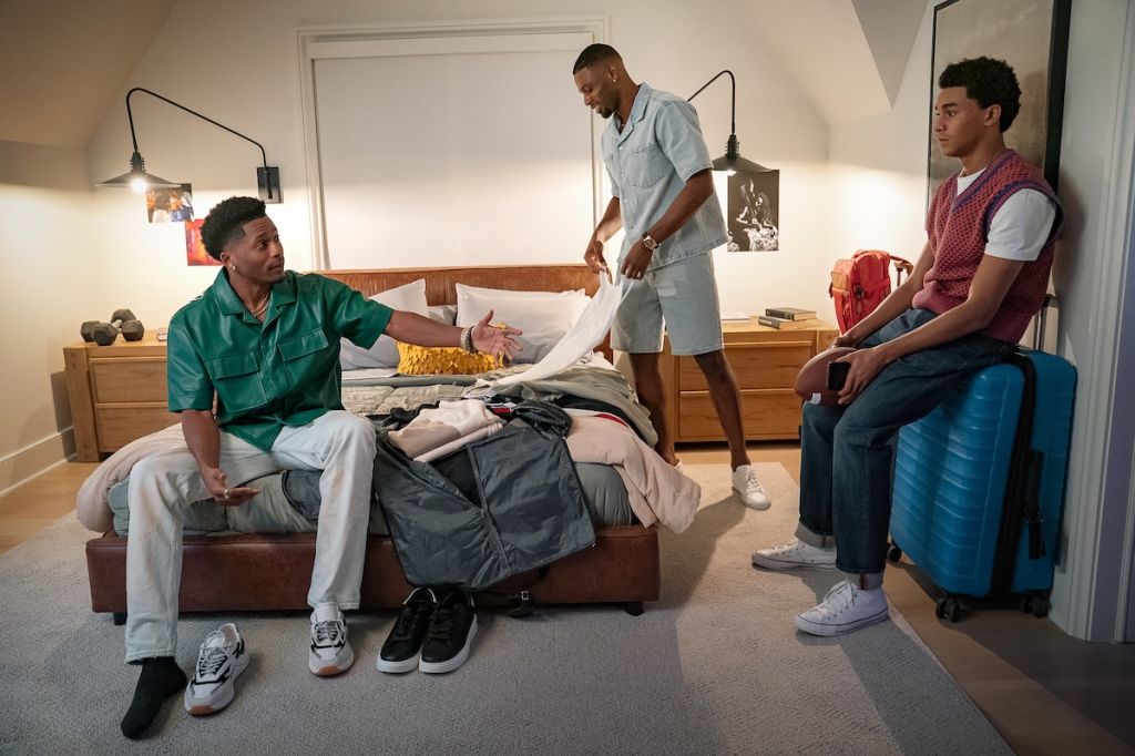 Three young men, one lying on a bed and two sitting, in a bedroom setting with various personal items and decor.