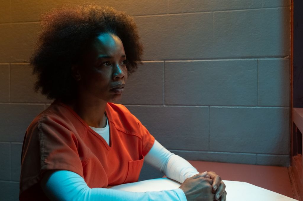 A person in an orange prison uniform sitting alone in a dimly lit room, looking pensive.